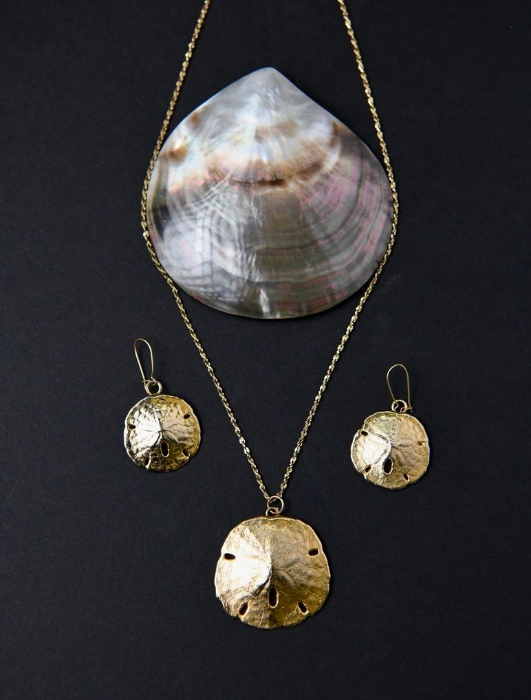 Mother of pearl shell and gold sand dollar pendant necklace and earrings displayed on dark surface.