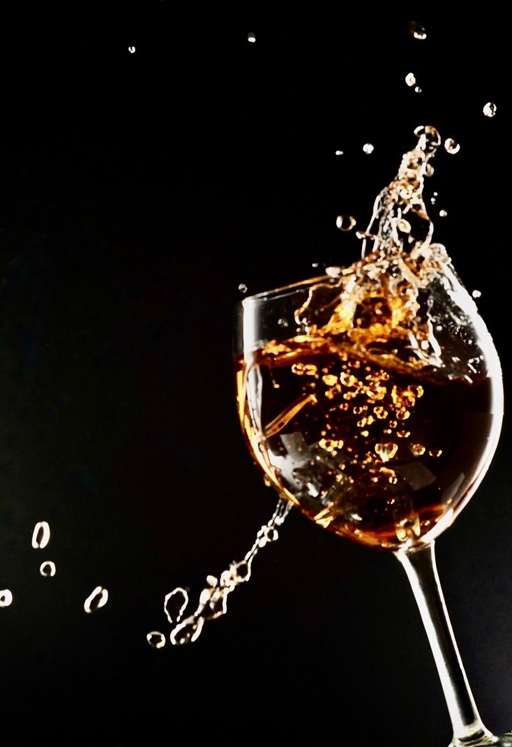 High-speed capture of liquid splashing out of a wine glass against dark background.