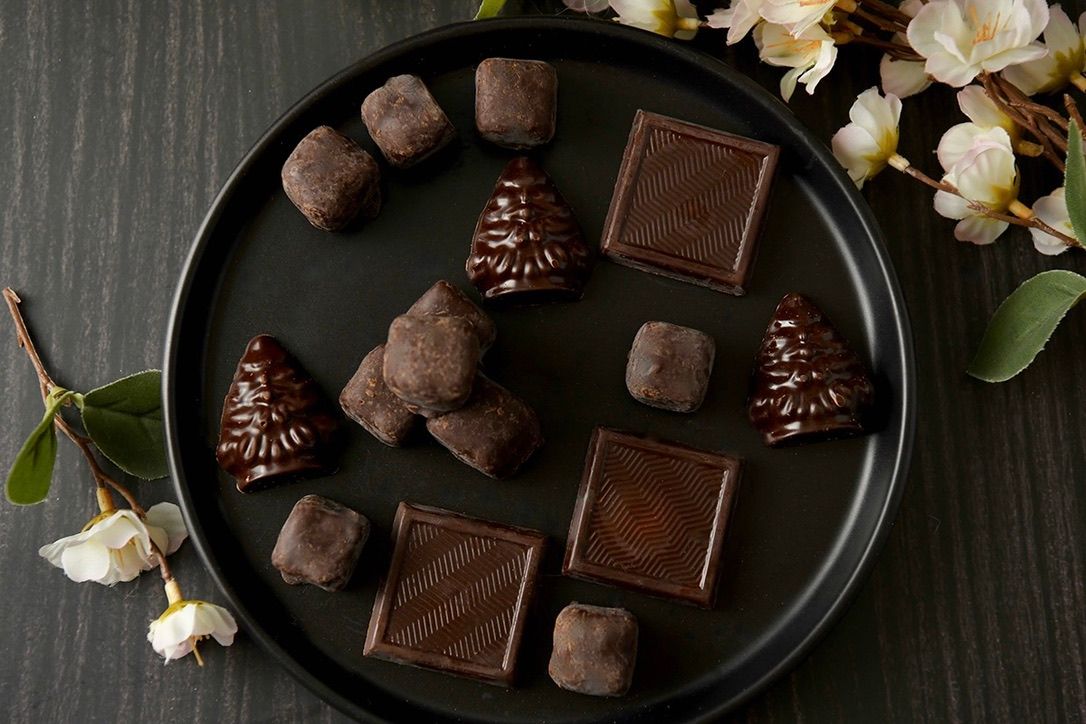 Artisanal chocolate truffles and squares displayed on dark plate with flowering branches.