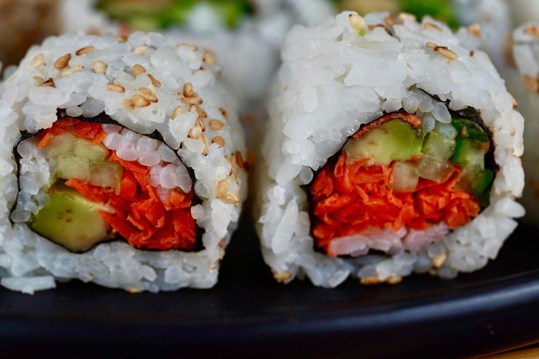 Close-up of fresh sushi rolls with rice, avocado and carrots on black plate.