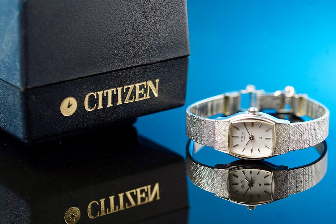 Elegant silver Citizen watch and box displayed on reflective blue surface.
