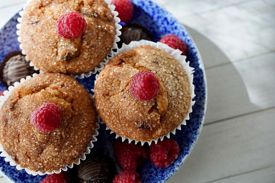 Sugar-dusted muffins garnished with fresh raspberries served on a blue patterned plate.