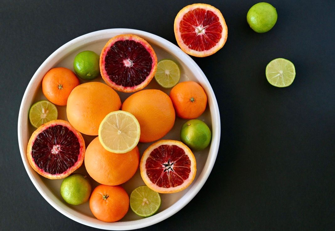 Fresh citrus fruits including oranges, blood oranges, and limes arranged in white bowl.