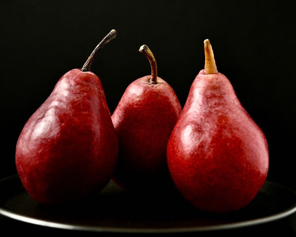 Fresh red pears arranged in a line on black surface with dramatic lighting.