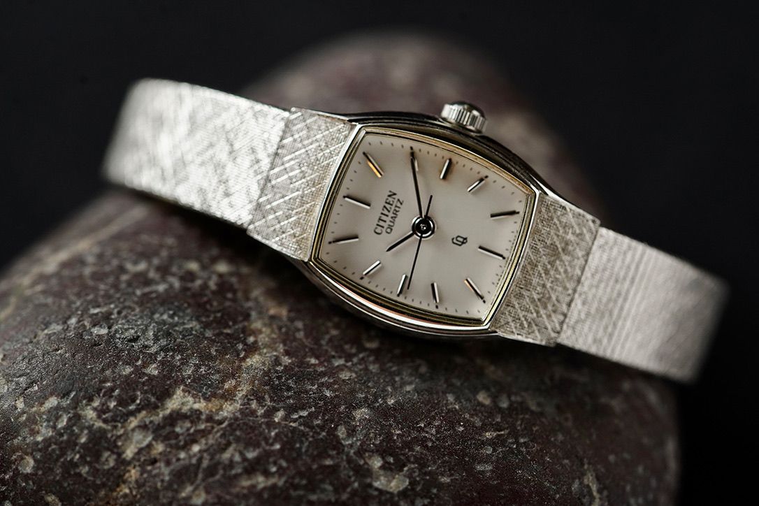 Vintage silver watch with mesh band photographed in dramatic lighting.