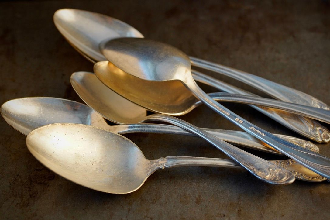 Vintage silver spoons and utensils arranged artistically with dramatic lighting.