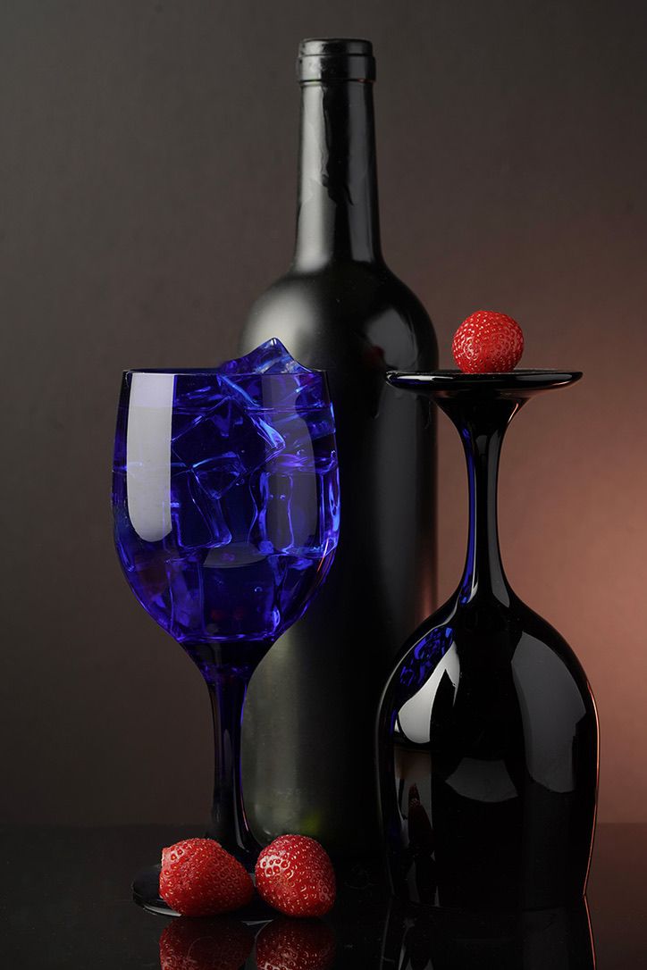Dark wine bottles with blue glass and red strawberries in moody lighting.