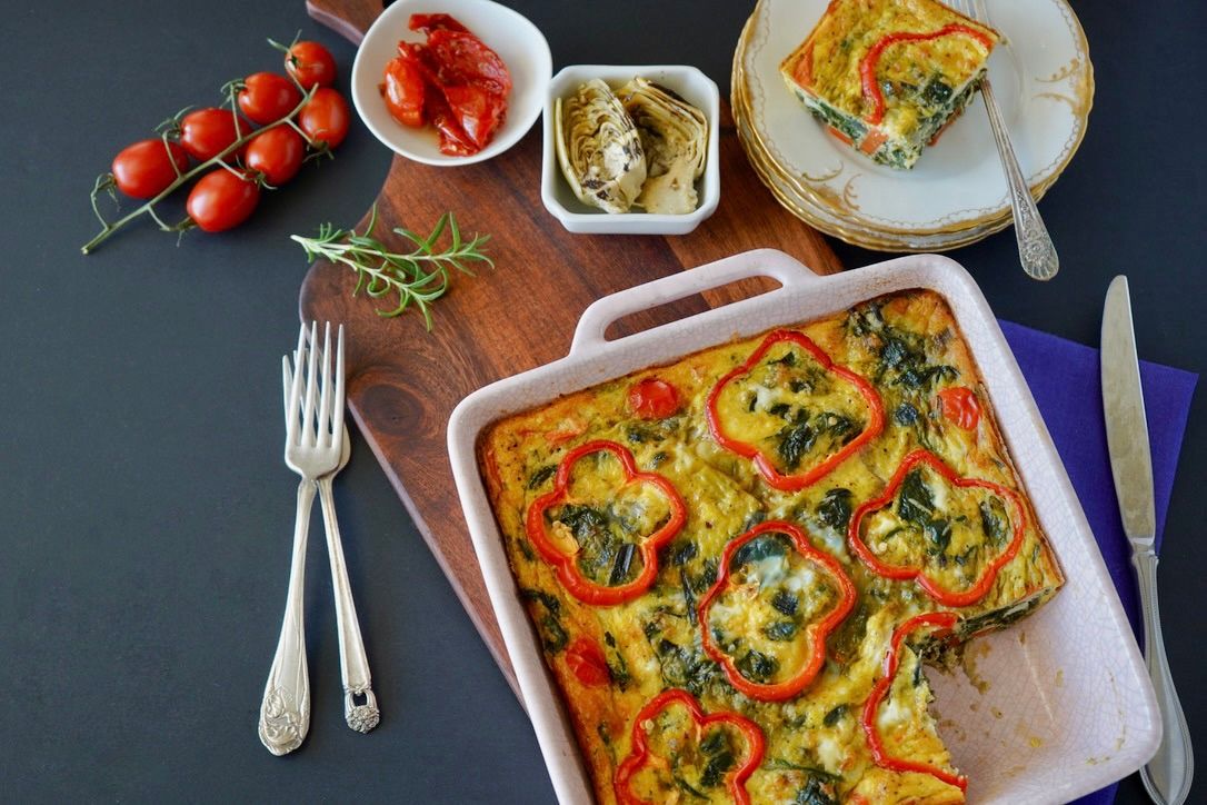 Colorful vegetable frittata with fresh herbs served on a rustic wooden board.