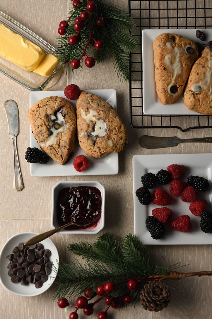Holiday scones with berries and chocolate served with butter and jam on white plates.