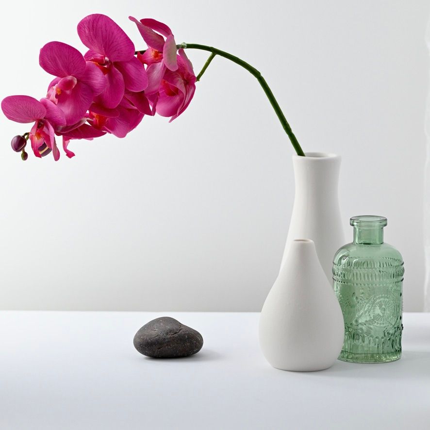 Pink orchids in white vase with vintage green glass bottles on white background.