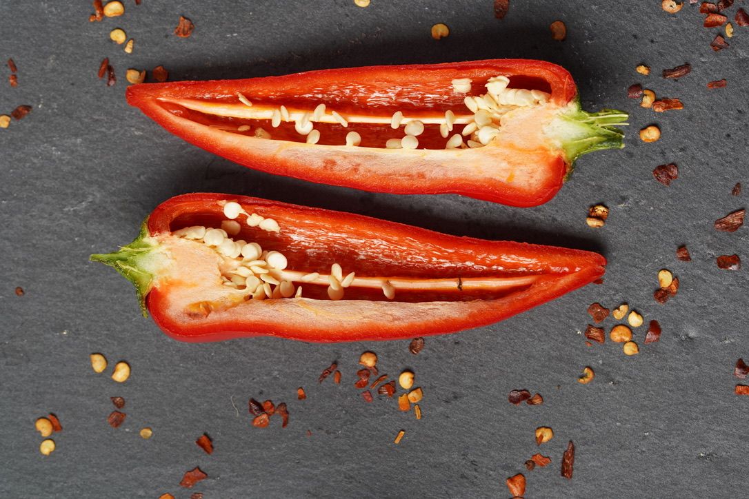 Sliced red bell peppers on dark slate surface showing seeds and inner texture.