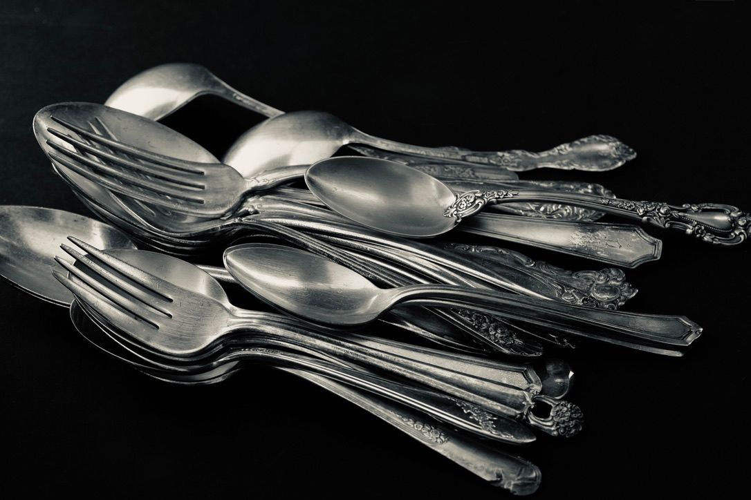 Collection of vintage silverware arranged dramatically on black background.