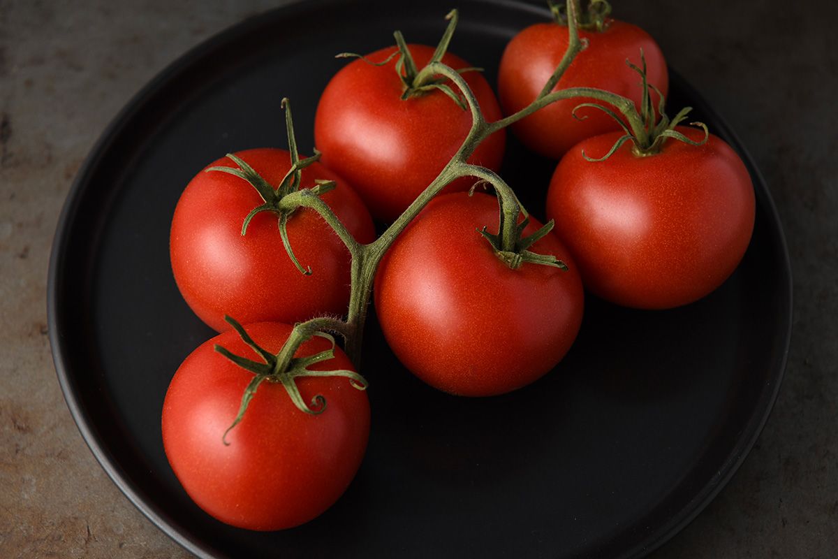 Fresh ripe red tomatoes on vine arranged on black plate against dark background.