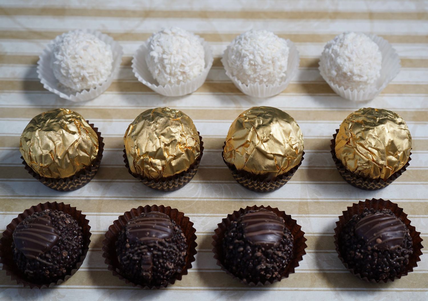 Row of chocolate truffles in gold and white wrappers displayed on striped surface.