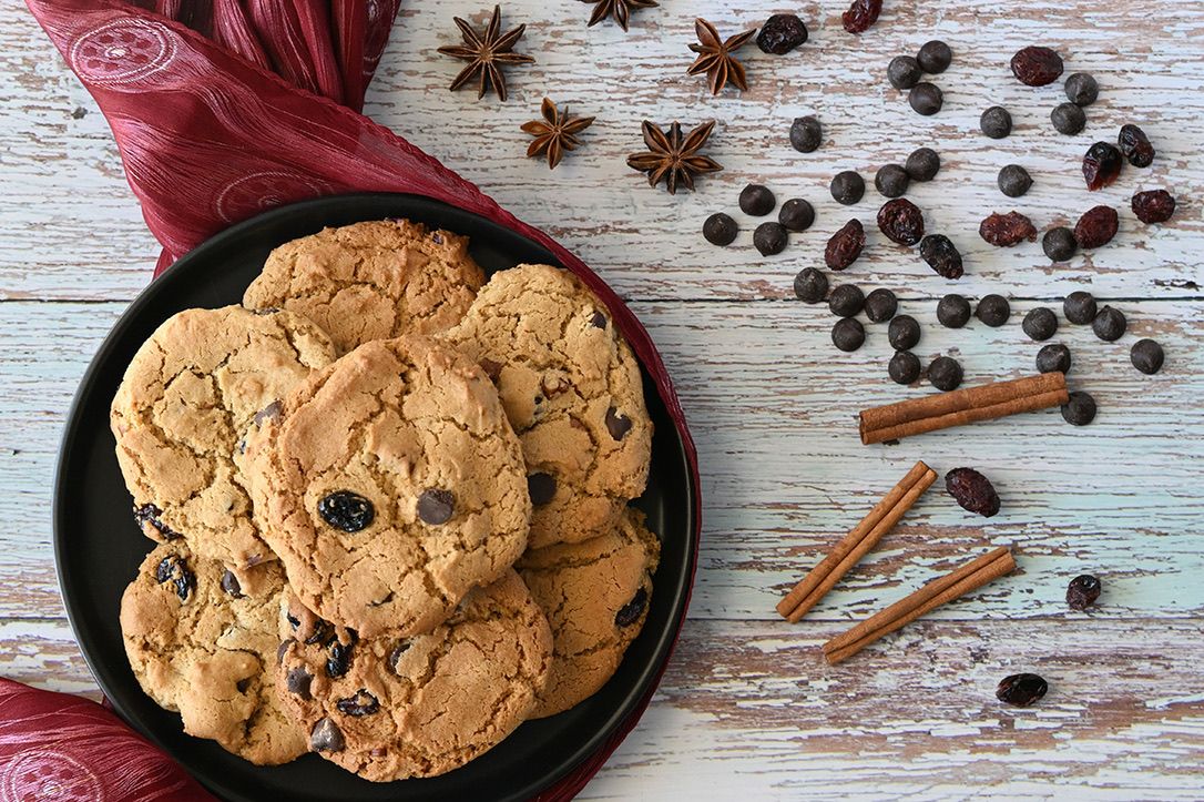 Chocolate chip cookies in cast iron skillet with spices and chocolate chips scattered nearby.