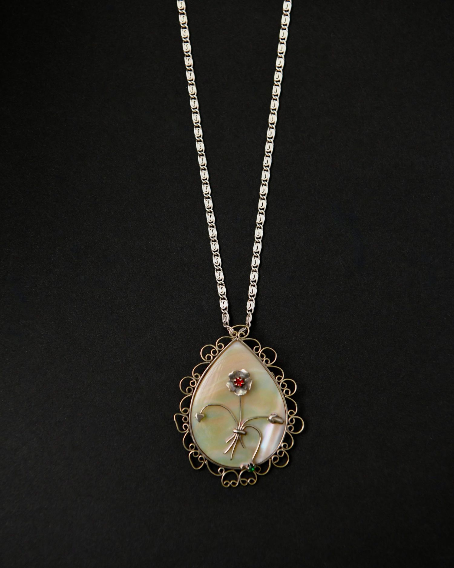 Delicate silver necklace with mother of pearl pendant displayed on black background.