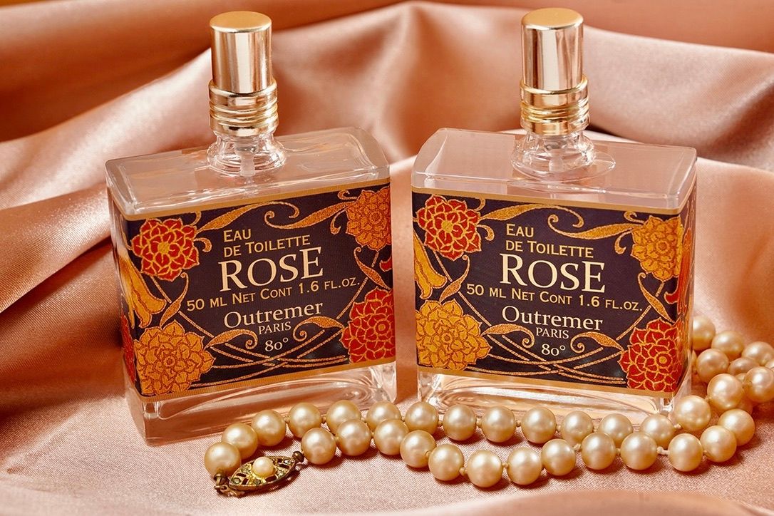 Two vintage-style rose perfume bottles with ornate designs displayed with a pearl necklace on pink satin fabric.