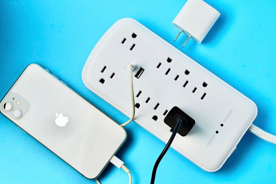 White power strip charging station with iPhone and accessories on blue background.