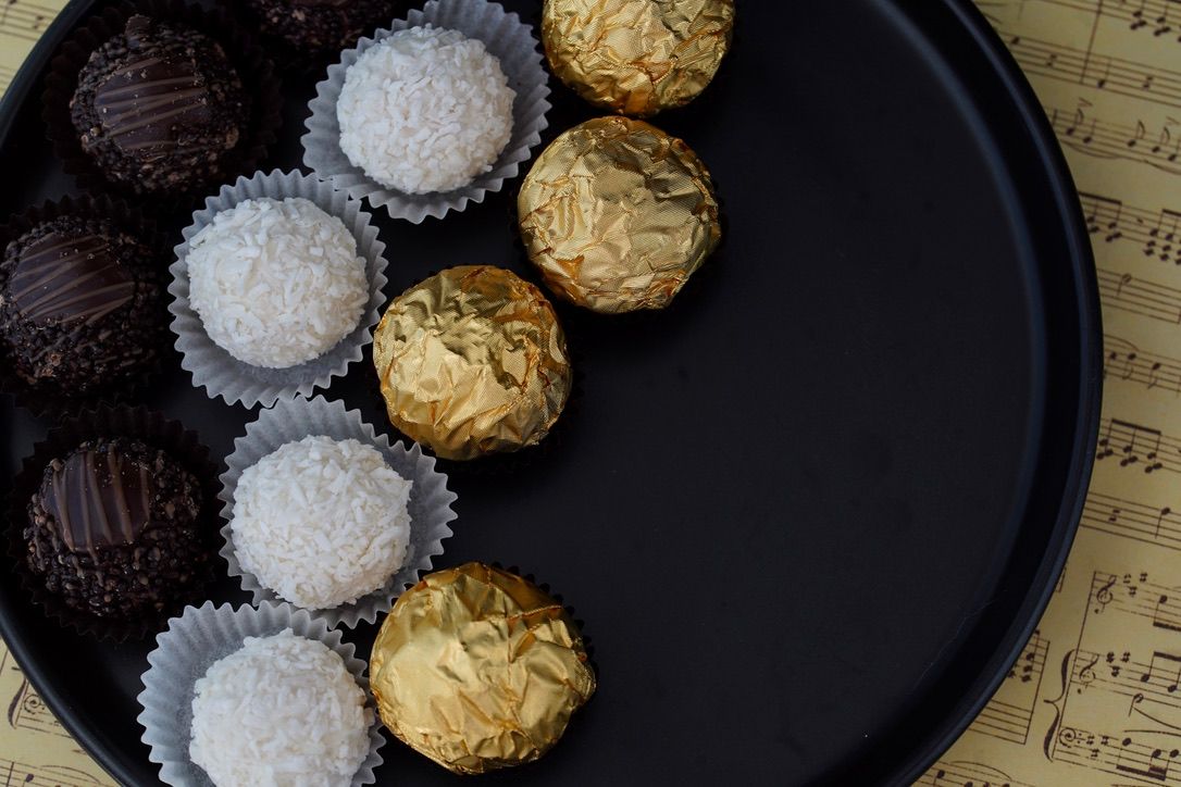 Elegant chocolate truffles in gold and white wrappers arranged on dark plate.