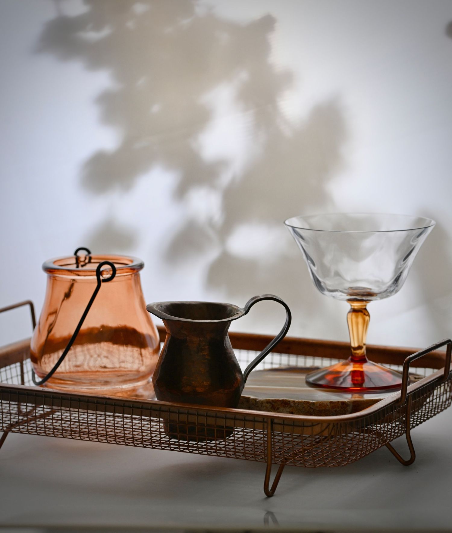 Copper pitcher, glass and glass candle holder on a metal serving tray with dramatic shadow play.