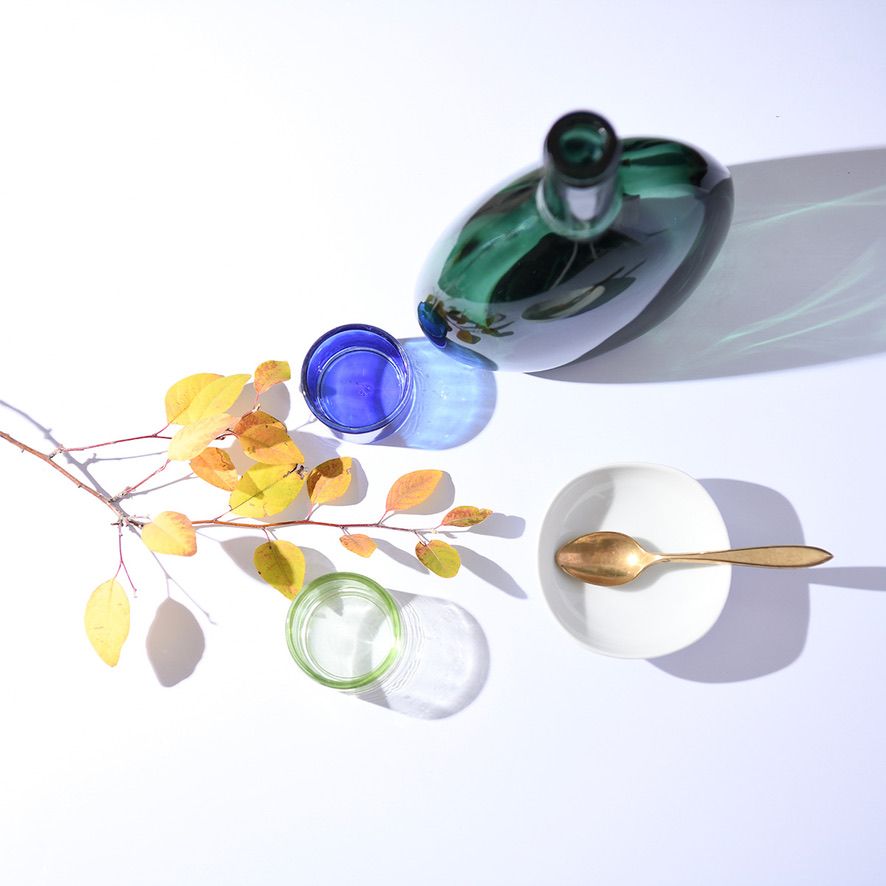 Green glass bottle with colorful marbles and autumn leaves casting shadows in bright light.