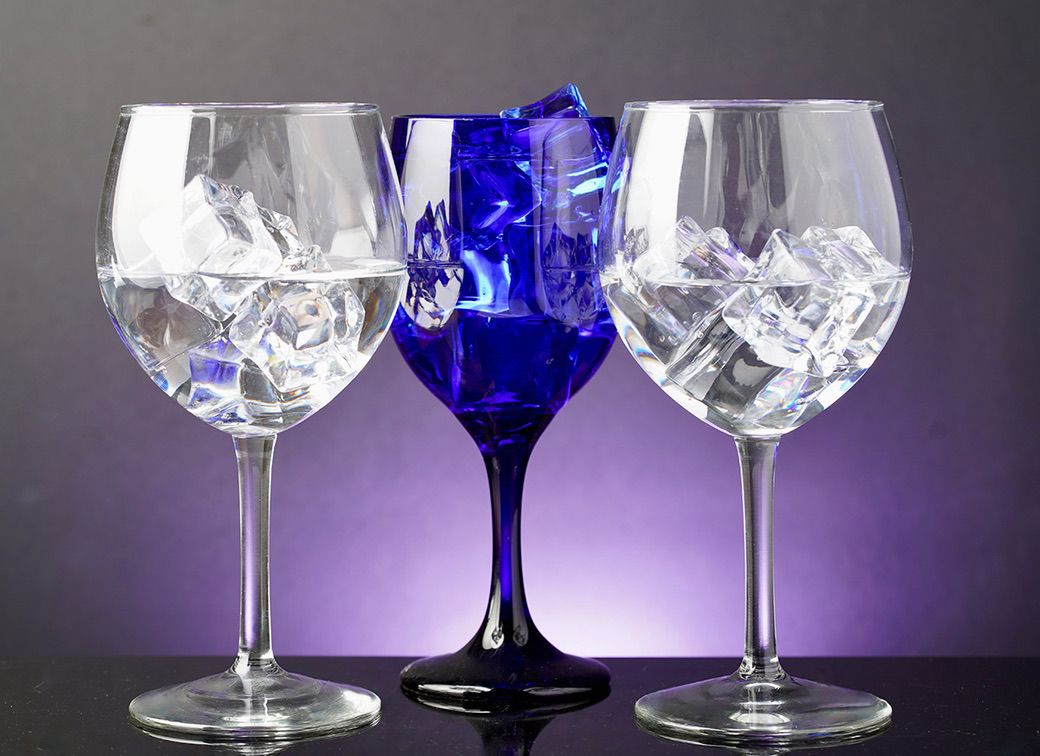 Three wine glasses with intricate crystal patterns, two clear and one cobalt blue, against purple background.
