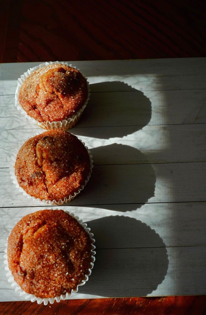 Fresh baked muffins with cinnamon sugar coating cast dramatic shadows on a rustic wooden surface.