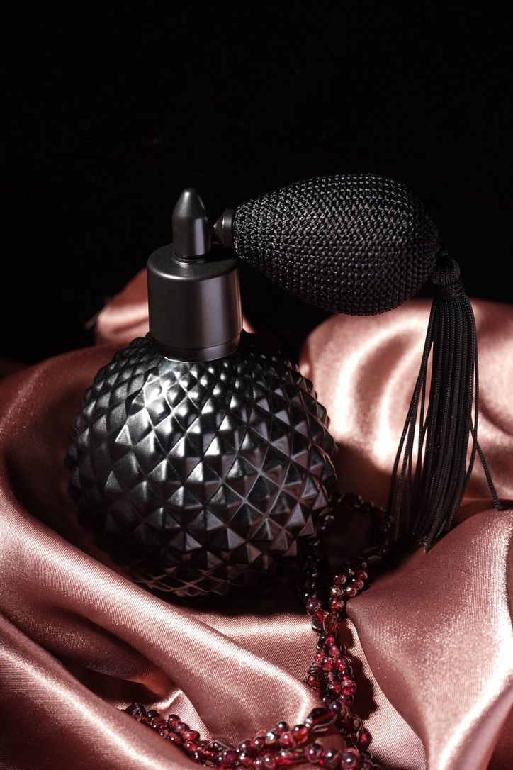 Vintage black perfume atomizer with tassel on pink silk fabric with beaded necklace.