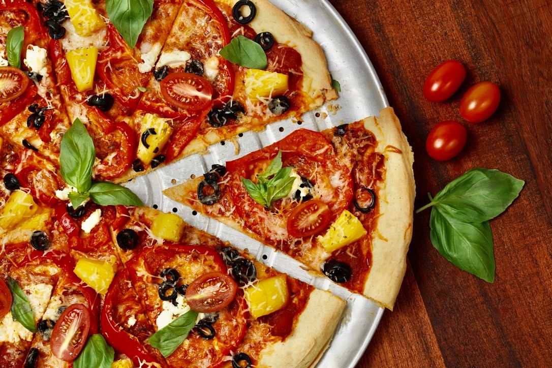 Homemade pizza topped with fresh vegetables, herbs and melted cheese cut into slices.