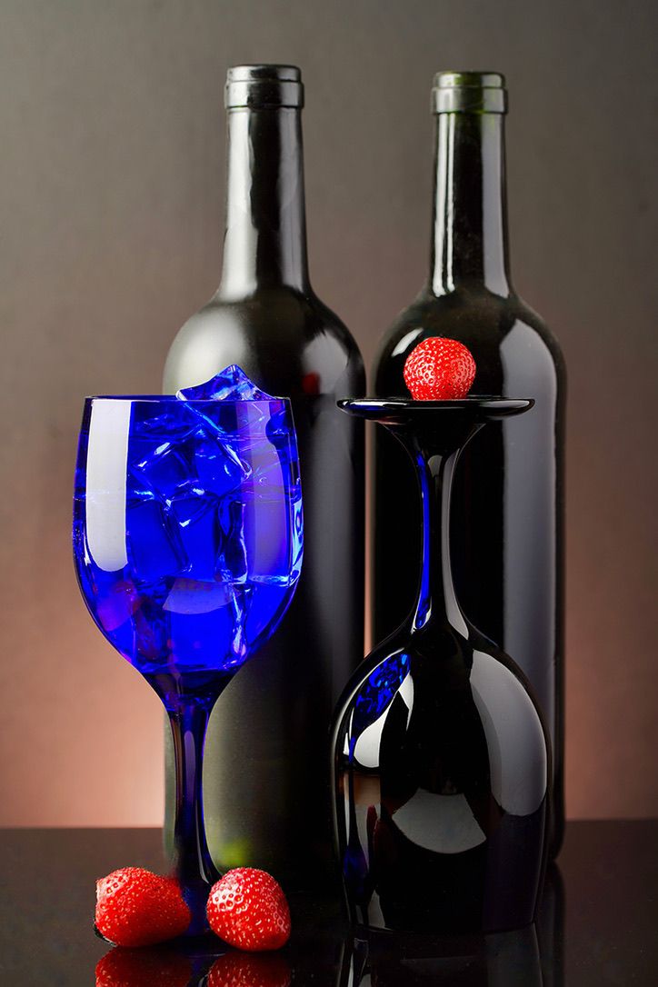 Still life with cobalt blue wine glasses, dark wine bottles, and fresh red strawberries against a dramatic dark background.
