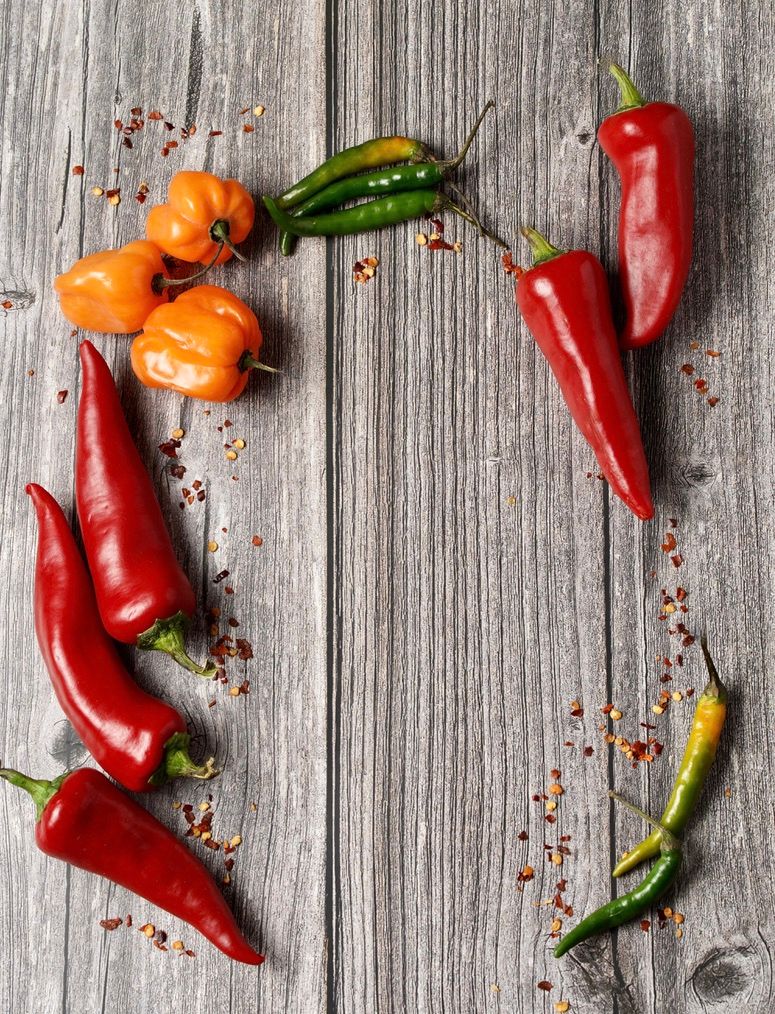 Assorted fresh chili peppers arranged on rustic wooden background with scattered spices.