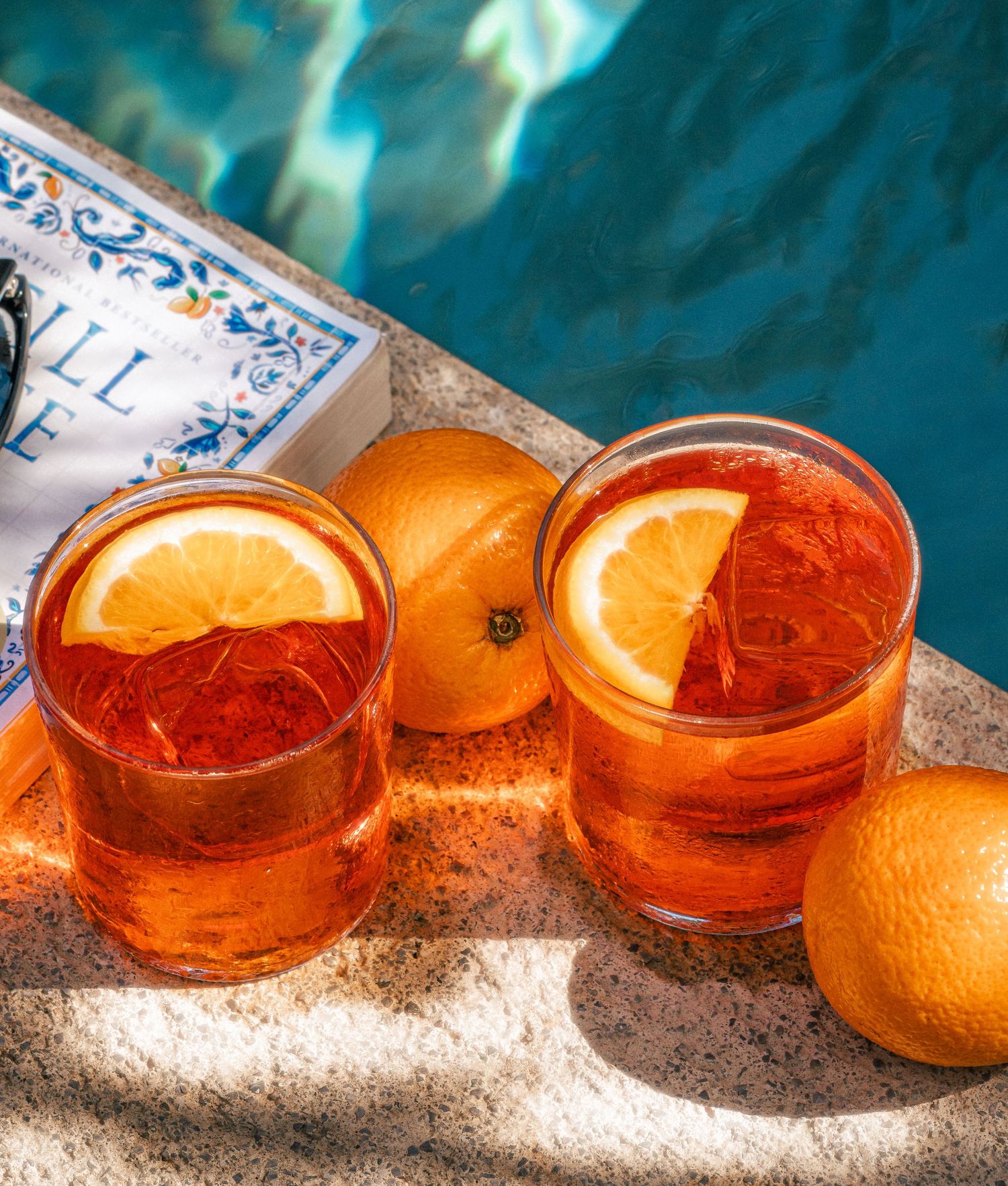 Orange cocktails garnished with citrus slices sit on a textured surface against a turquoise background.