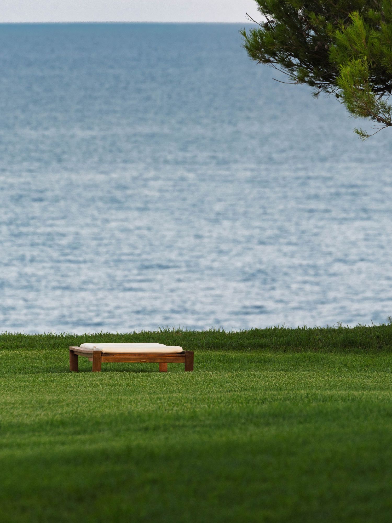 Manicured green lawn overlooking calm blue ocean waters on a sunny day.