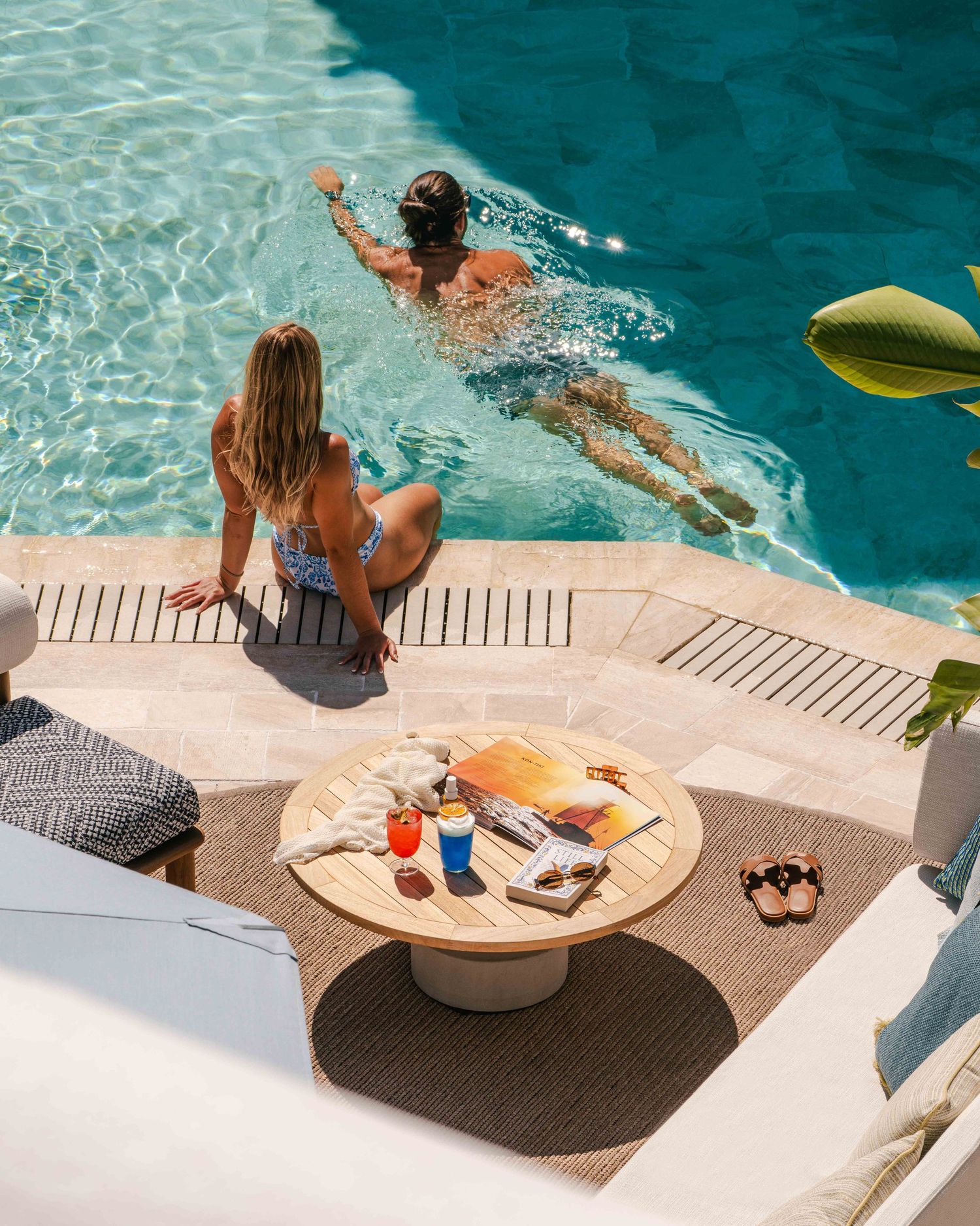 Pool scene with round wooden table and swimmers enjoying the crystal clear water.