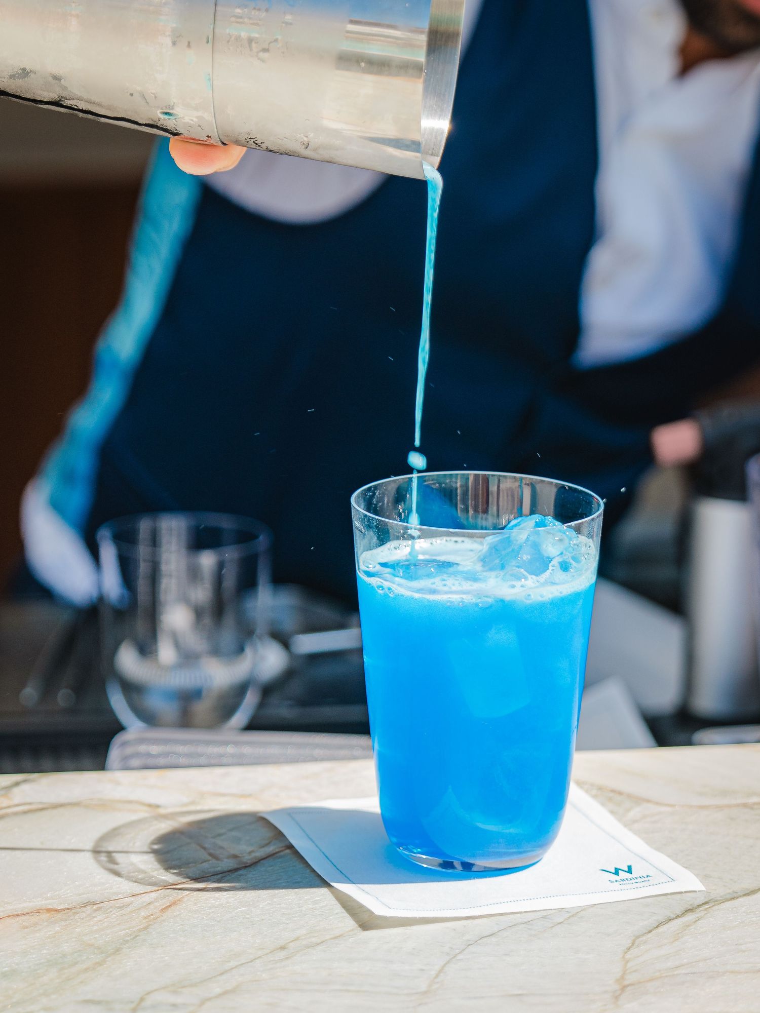 Vibrant blue liquid being carefully poured into a cocktail glass with ice.