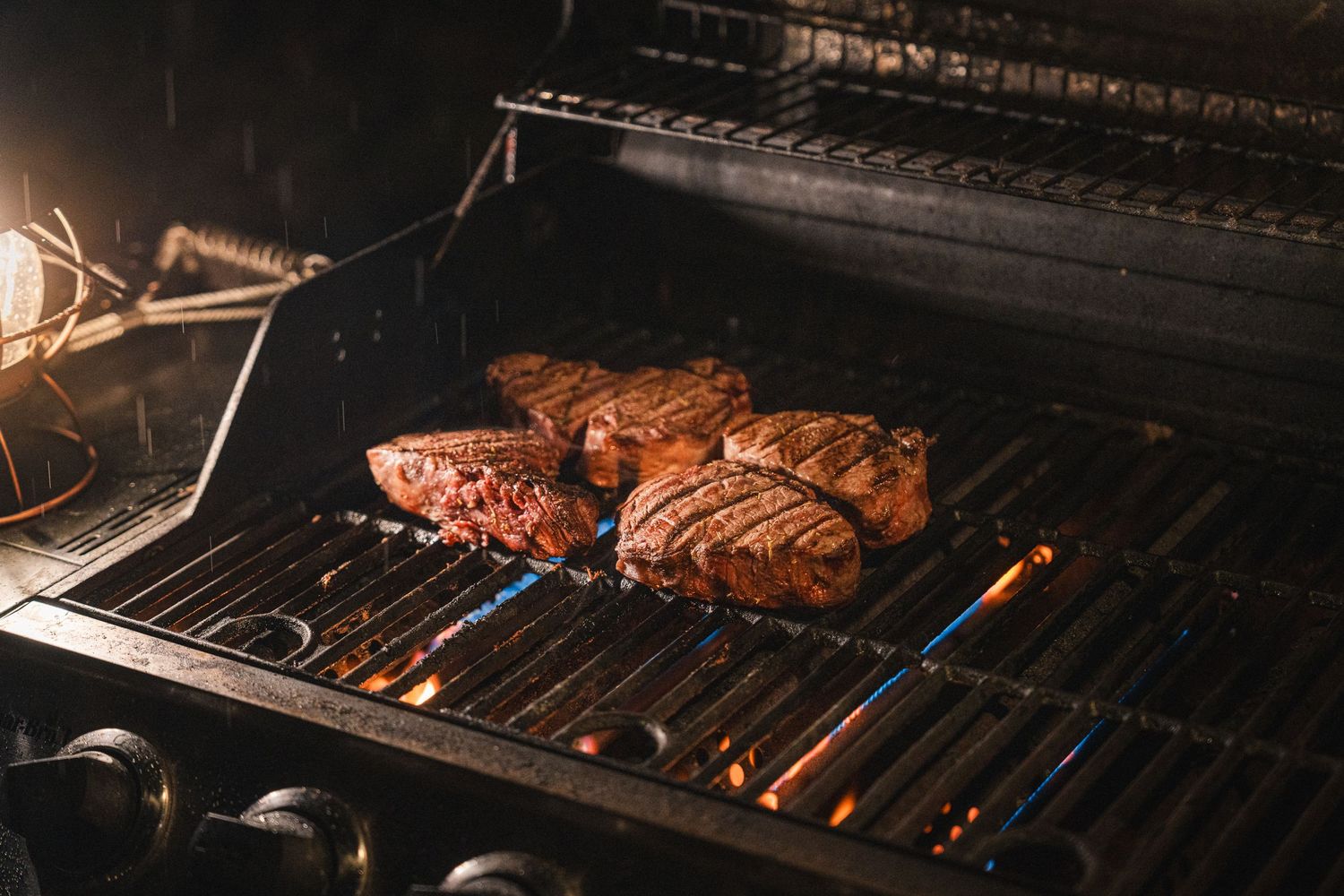 Two thick steaks sizzling on a hot indoor grill with flames visible through the metal grates.