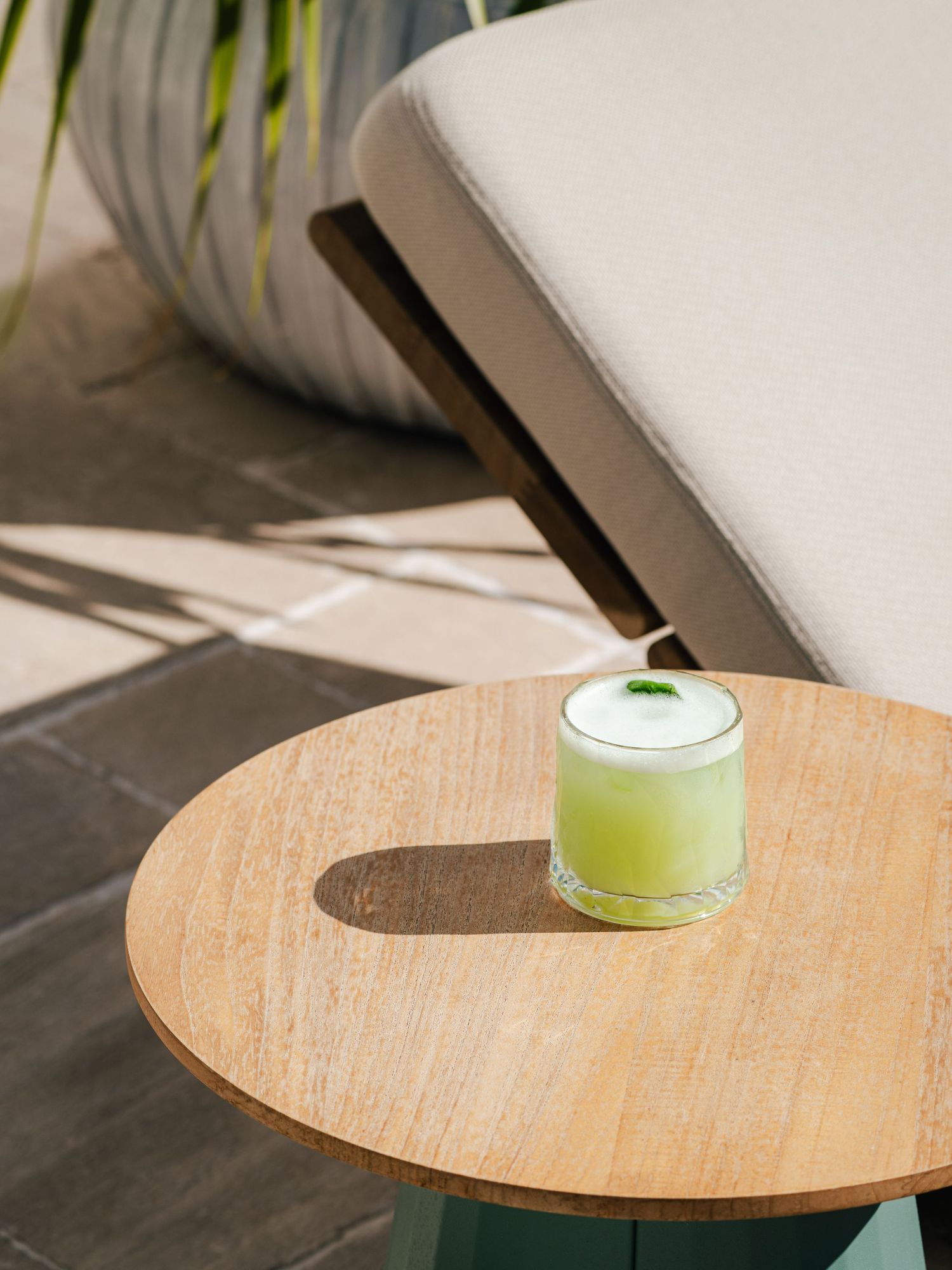 Wooden side table with a green beverage glass on top against a light background.