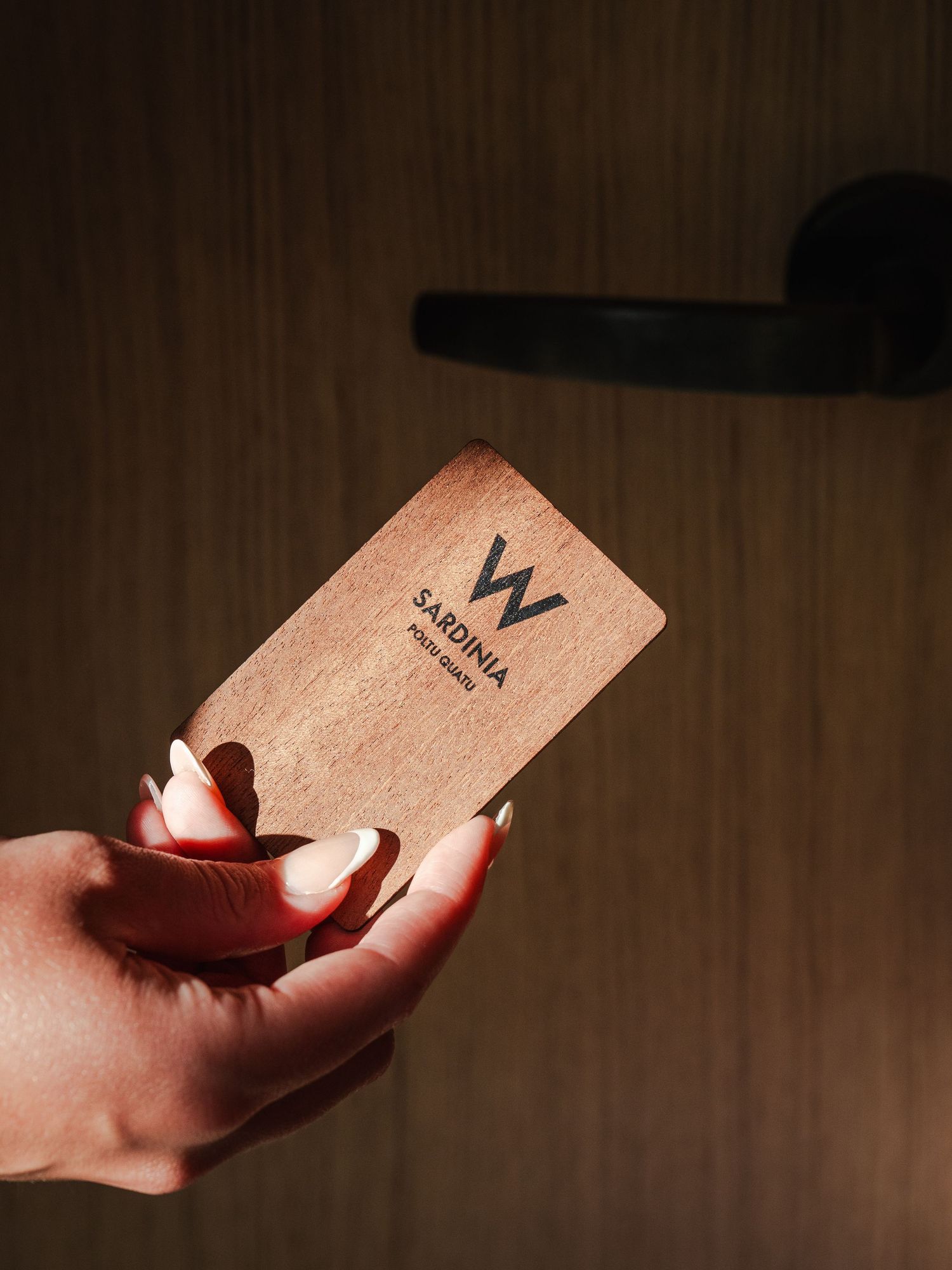 Hand holding a wooden hotel key card with W branding in dramatic lighting.