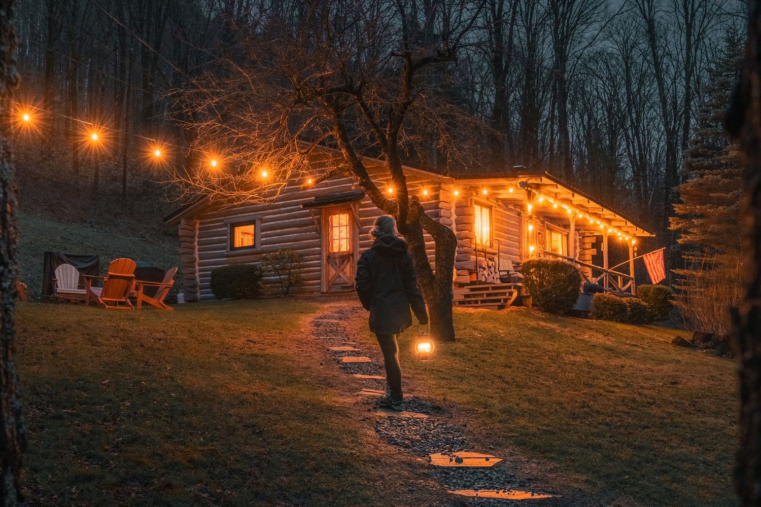 A cozy cabin illuminated at night with the Milky Way galaxy shining brightly in the starlit sky above.