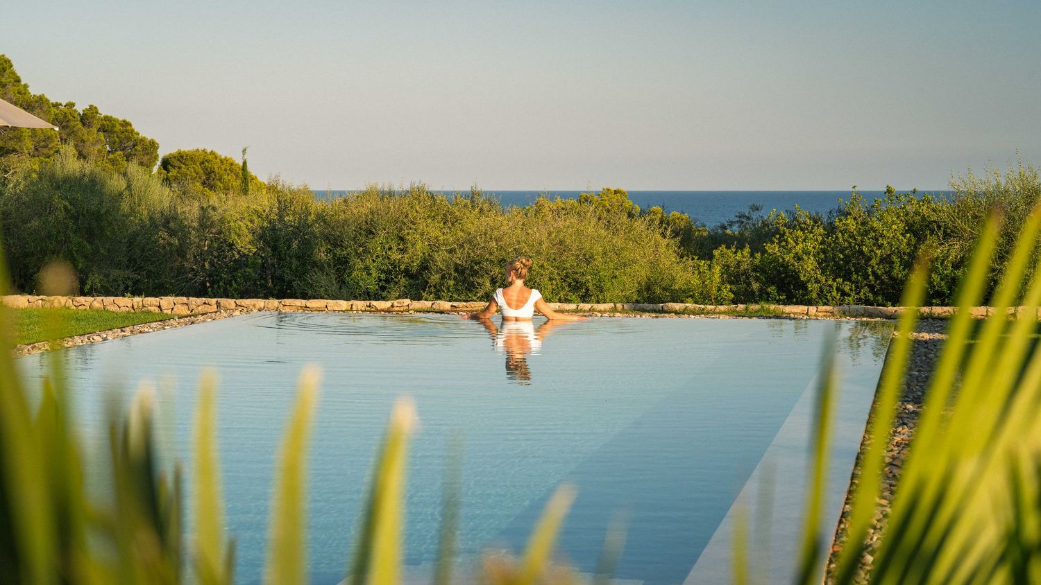 Serene infinity pool surrounded by Mediterranean vegetation with ocean views.
