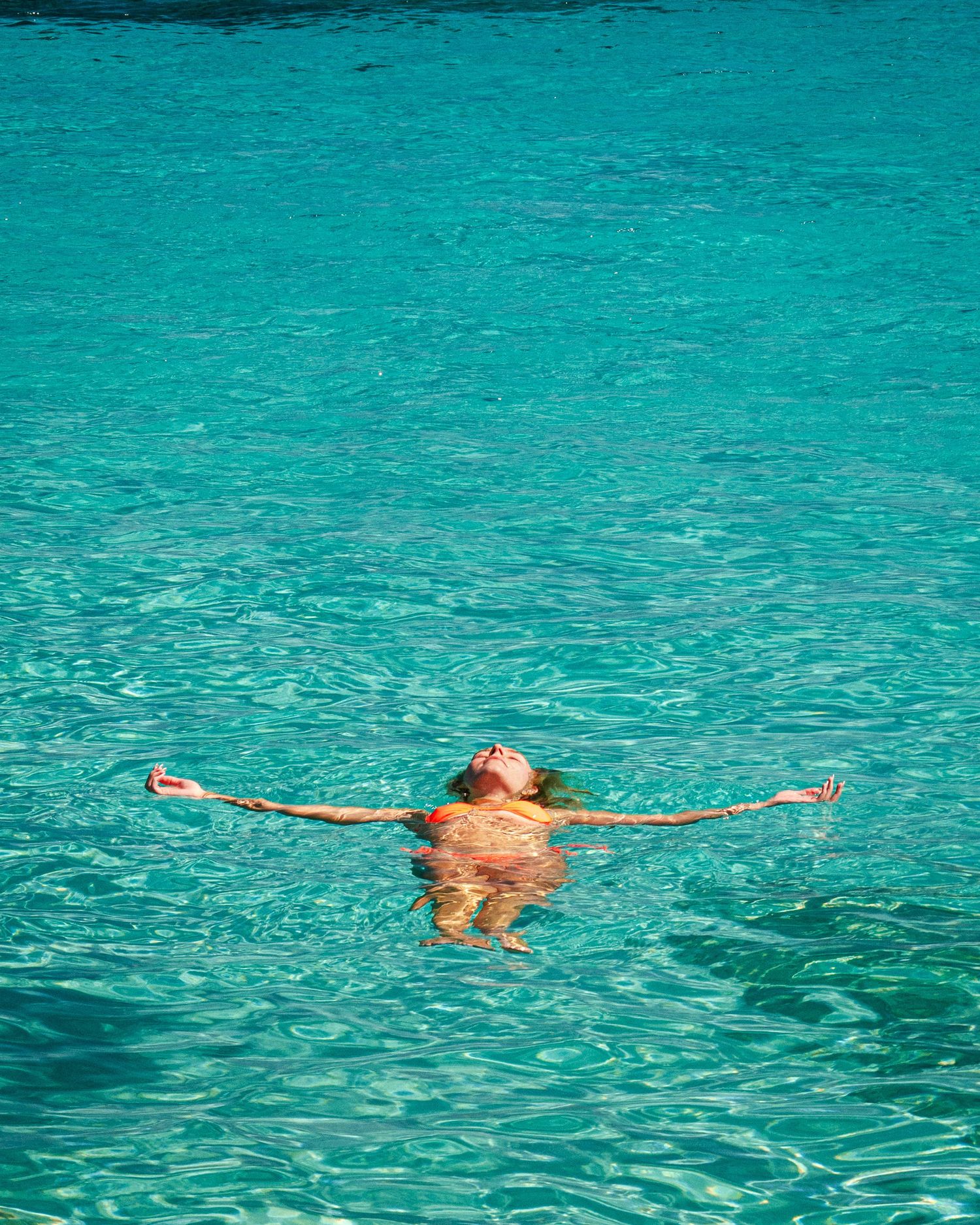 Person floating peacefully in crystal clear turquoise Mediterranean waters.