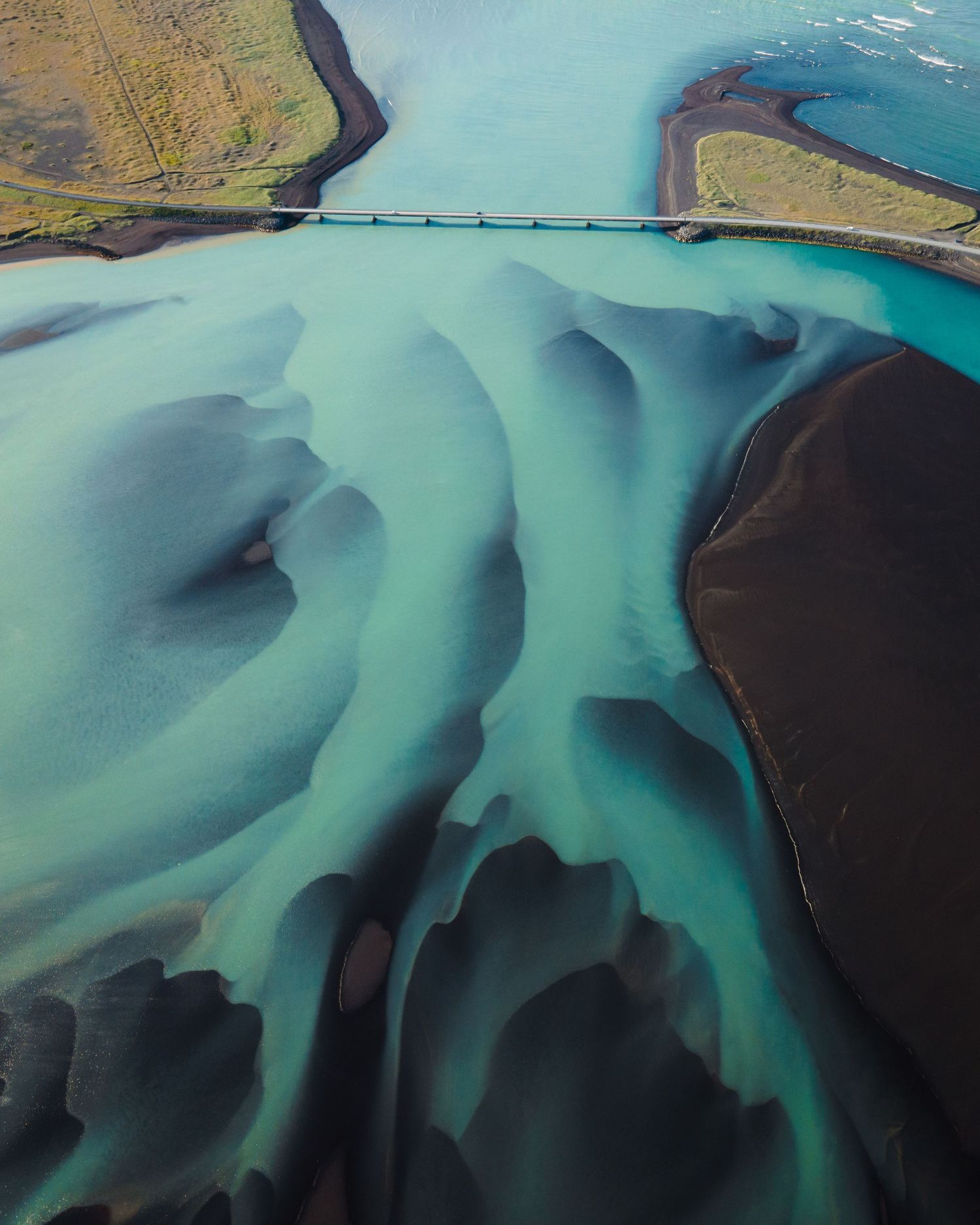 Aerial view of glacial river patterns creating abstract turquoise channels through dark landscape.