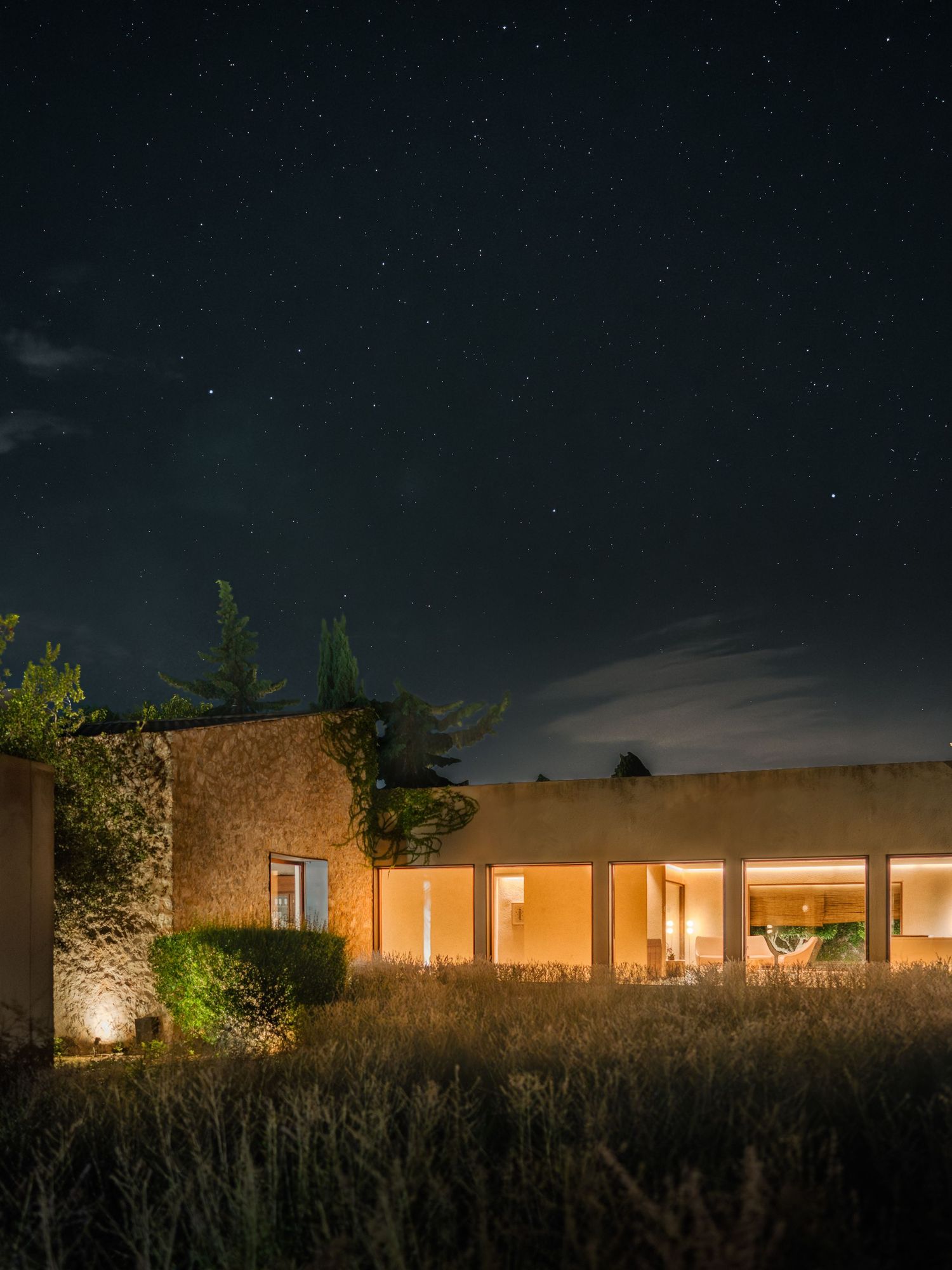 Desert home with lit windows glowing against dark night sky.