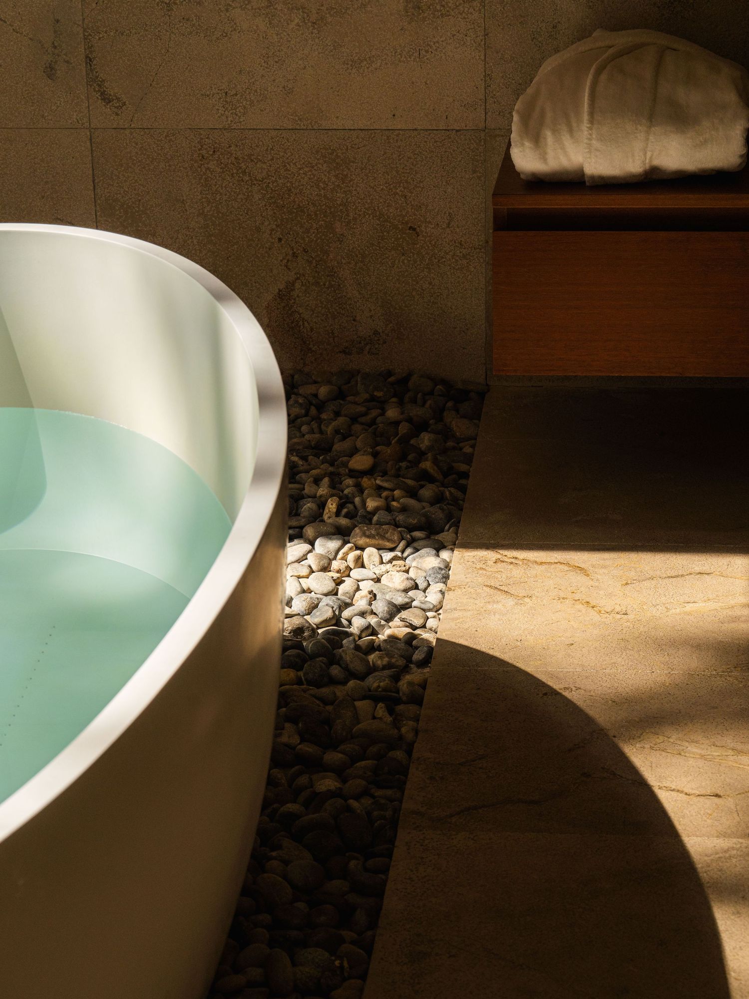 Modern white bathtub with pebble accents and dramatic lighting creating shadows.
