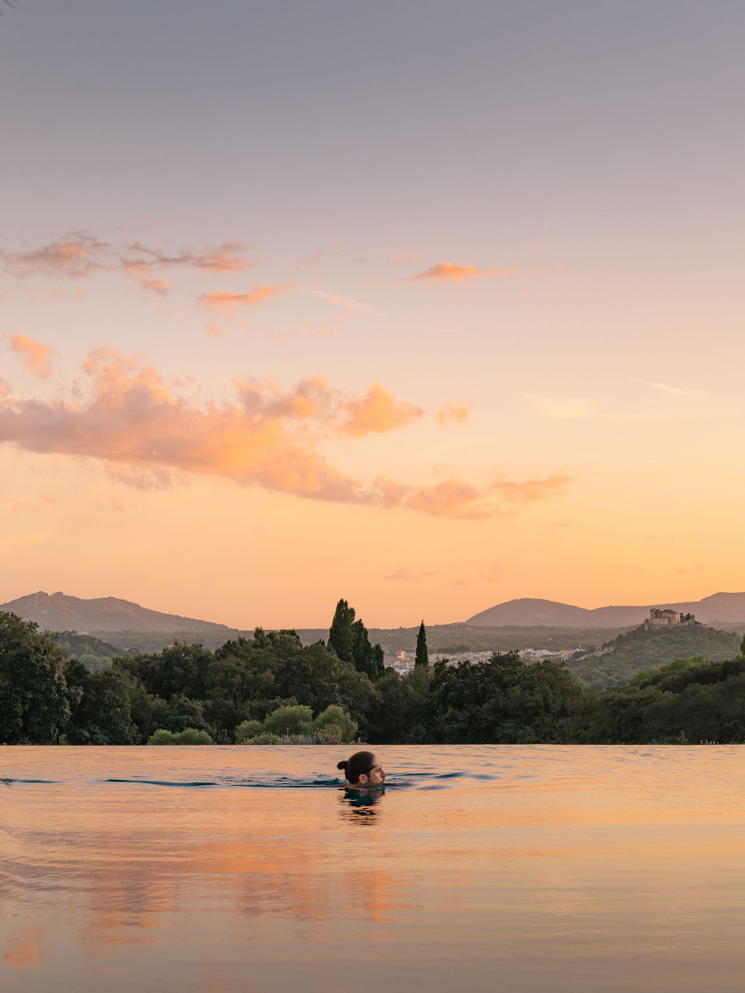 Serene lake landscape at sunset with mountains silhouetted against orange and pink sky.