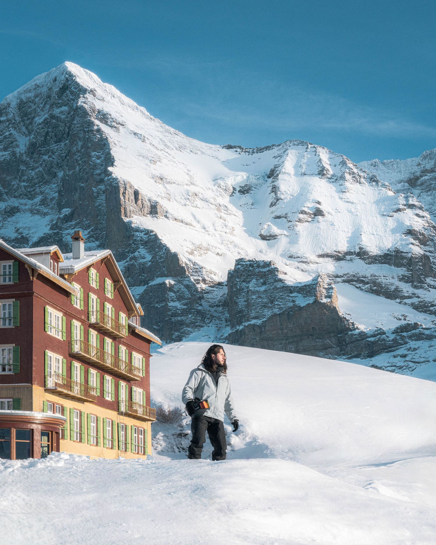Snow-covered alpine lodge beneath majestic mountain peaks in winter wonderland setting.