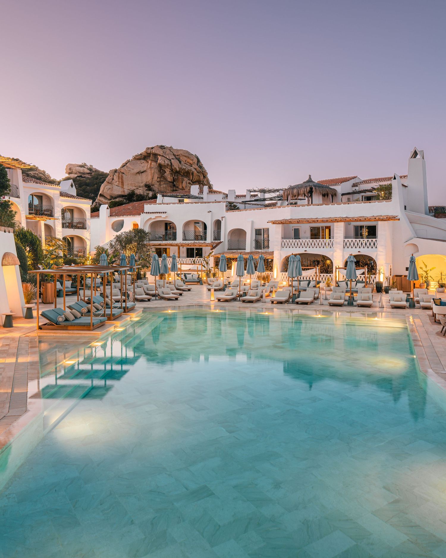 Mediterranean resort with white buildings and turquoise pool during sunset.