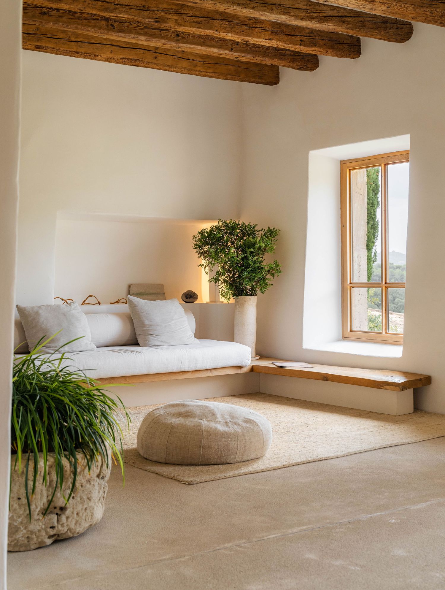 Serene white room with exposed beams, natural light, and comfortable floor cushions creating a zen atmosphere.