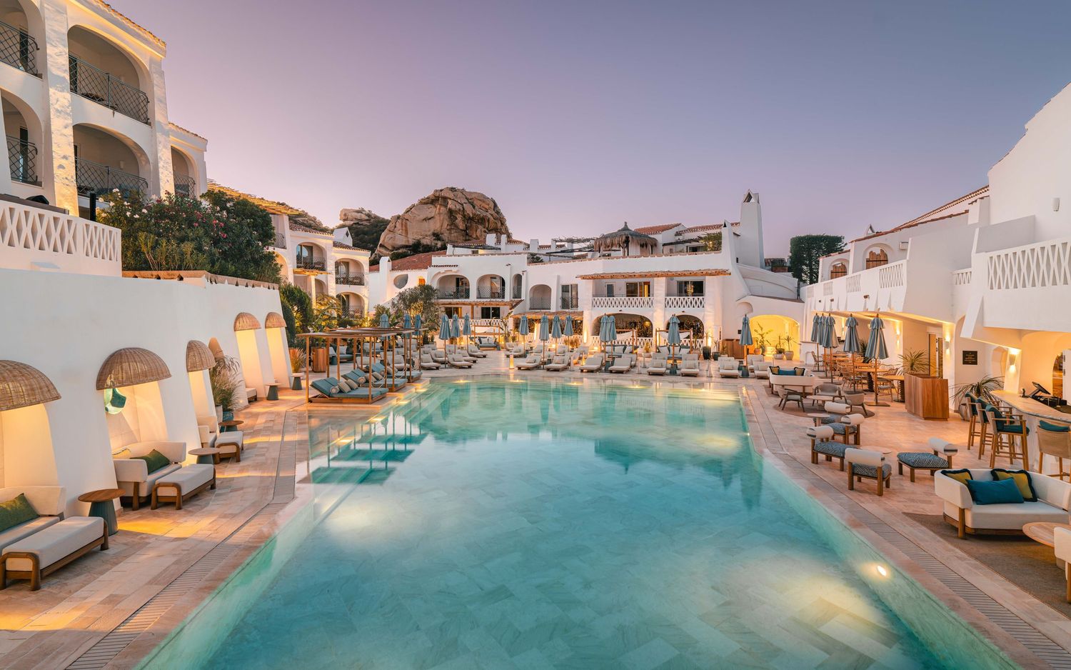 Luxury resort swimming pool with white buildings and ocean views at sunset.