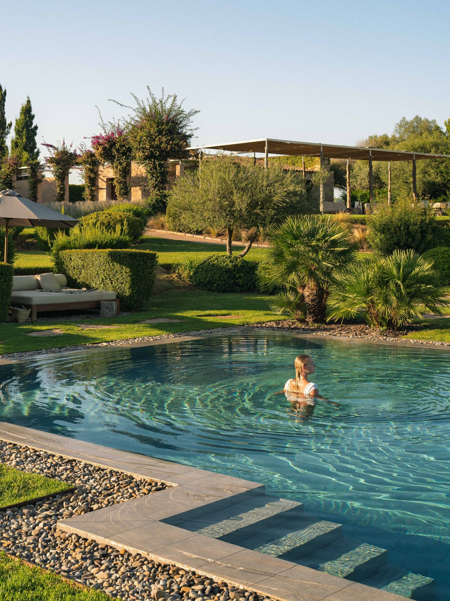 Luxurious infinity pool with stone border surrounded by Mediterranean garden landscape.